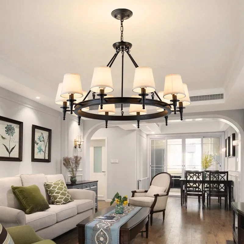 A modern classic chandelier with black metal and cream lampshades, hanging in a bright living room with light-colored furniture and decor